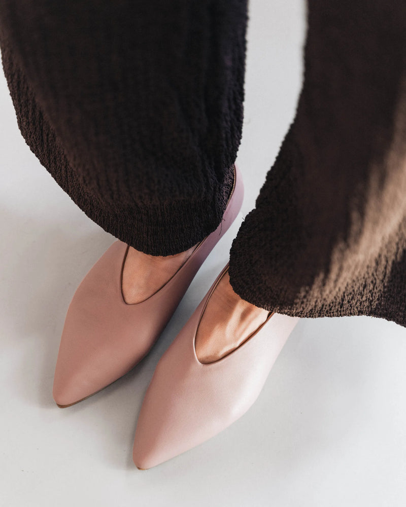 Leather pointed-toe flats, overhead view with black textured trousers. The Atelier Flat Dusty Mauve. Sizes 5–12.
