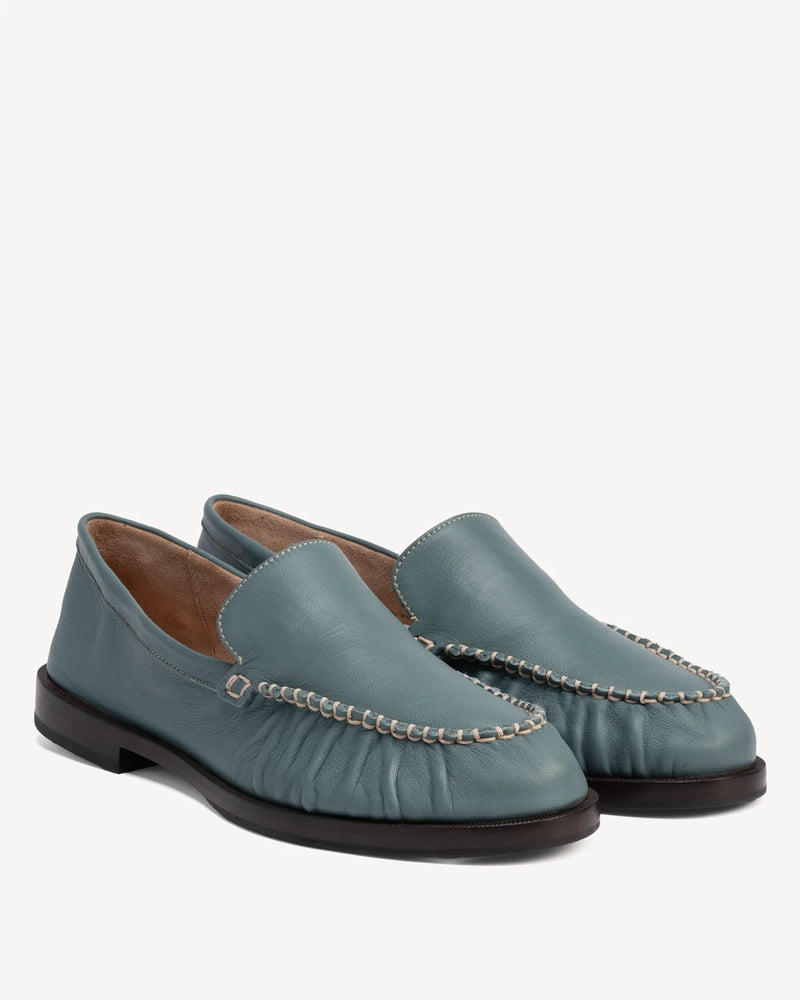 Angled pair of slip-on loafers with ruched vamp and chain trim. The Laid Back Loafer Storm. Sizes 5–12, wide available.