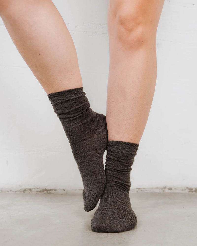 Feet crossed at the ankles showing the slouchy ribbed cuff detail. The Dressy Crew Sock Charcoal Melange.