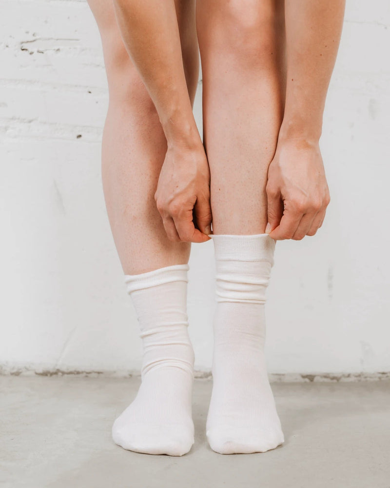 Close-up of hands pulling the ribbed cuff up over the ankle. The Dressy Crew Sock Alabaster 3-Pack.