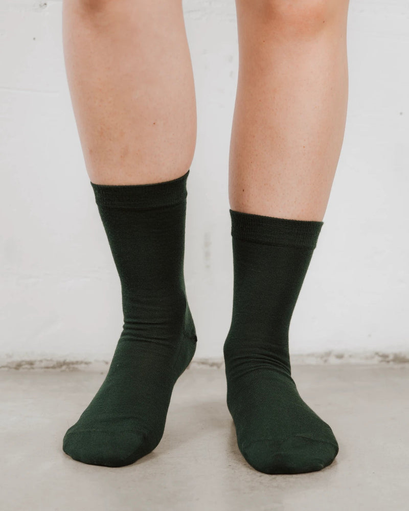 Front view on bare legs, soft wool knit with a ribbed cuff. The Dressy Crew Sock Balsam.