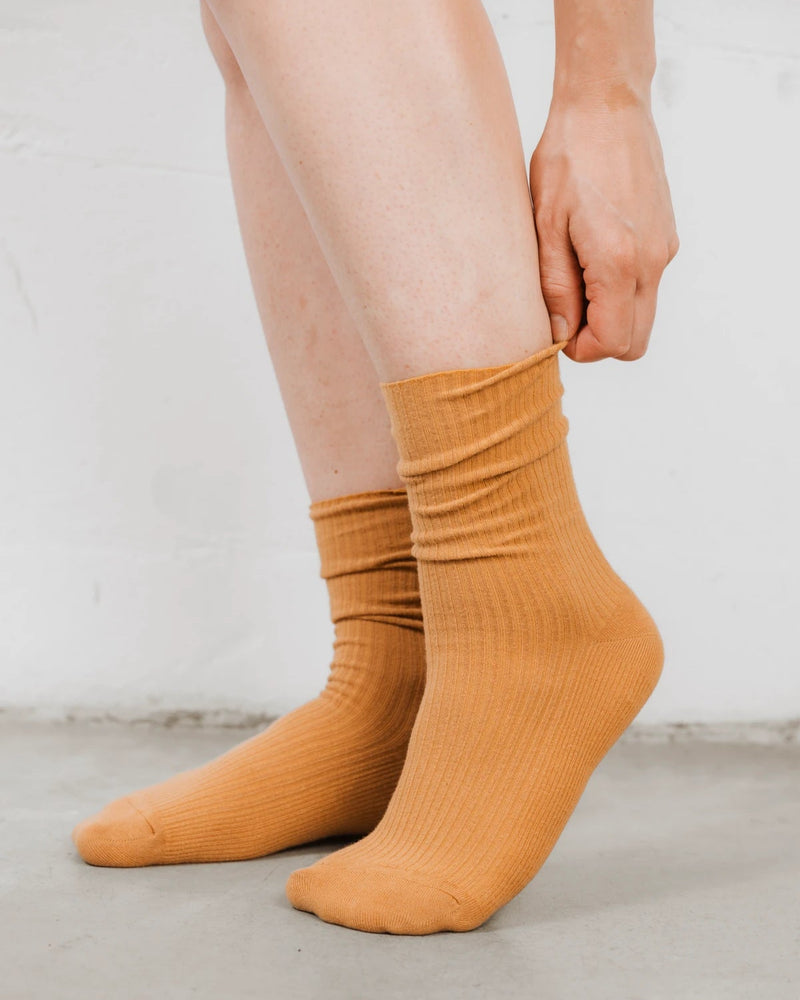 Close-up of a hand adjusting the ribbed cuff on a cotton-rich crew sock. The Ribbed Crew Sock Ochre.