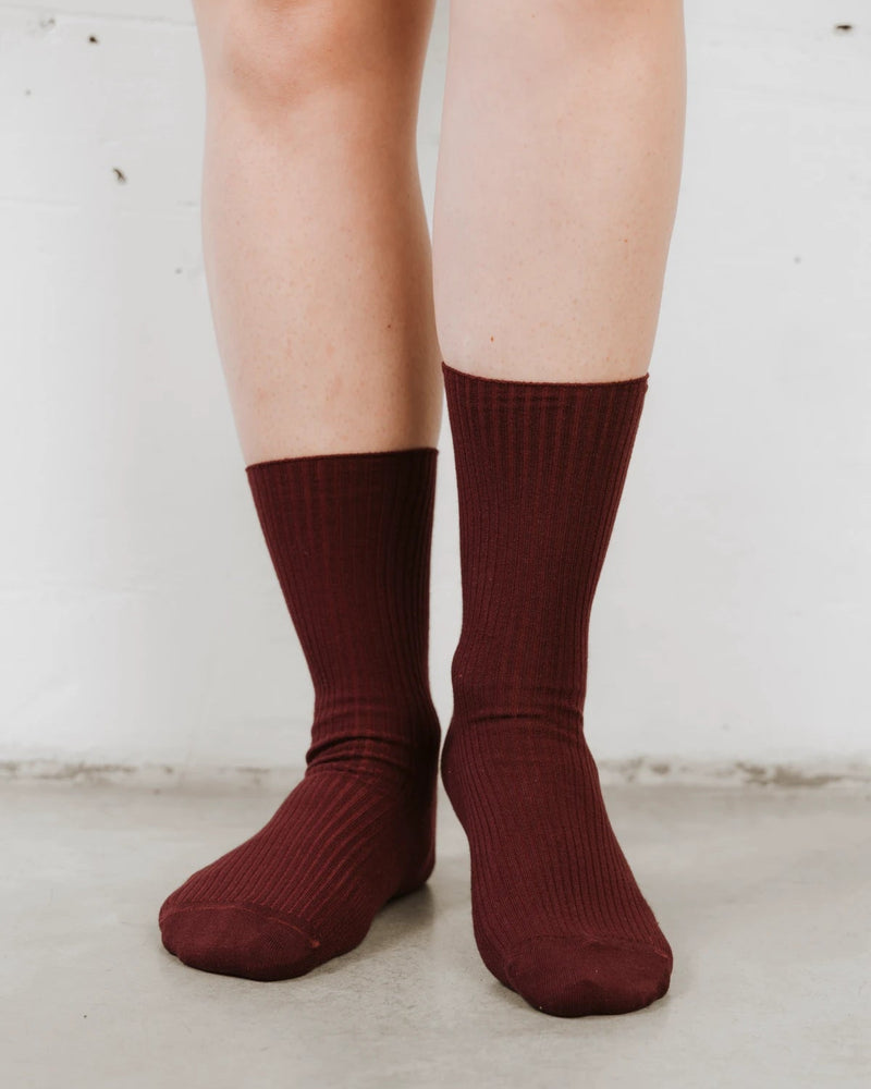 Close view of ribbed knit texture and folded cuff on bare legs. The Ribbed Crew Sock Sangria.