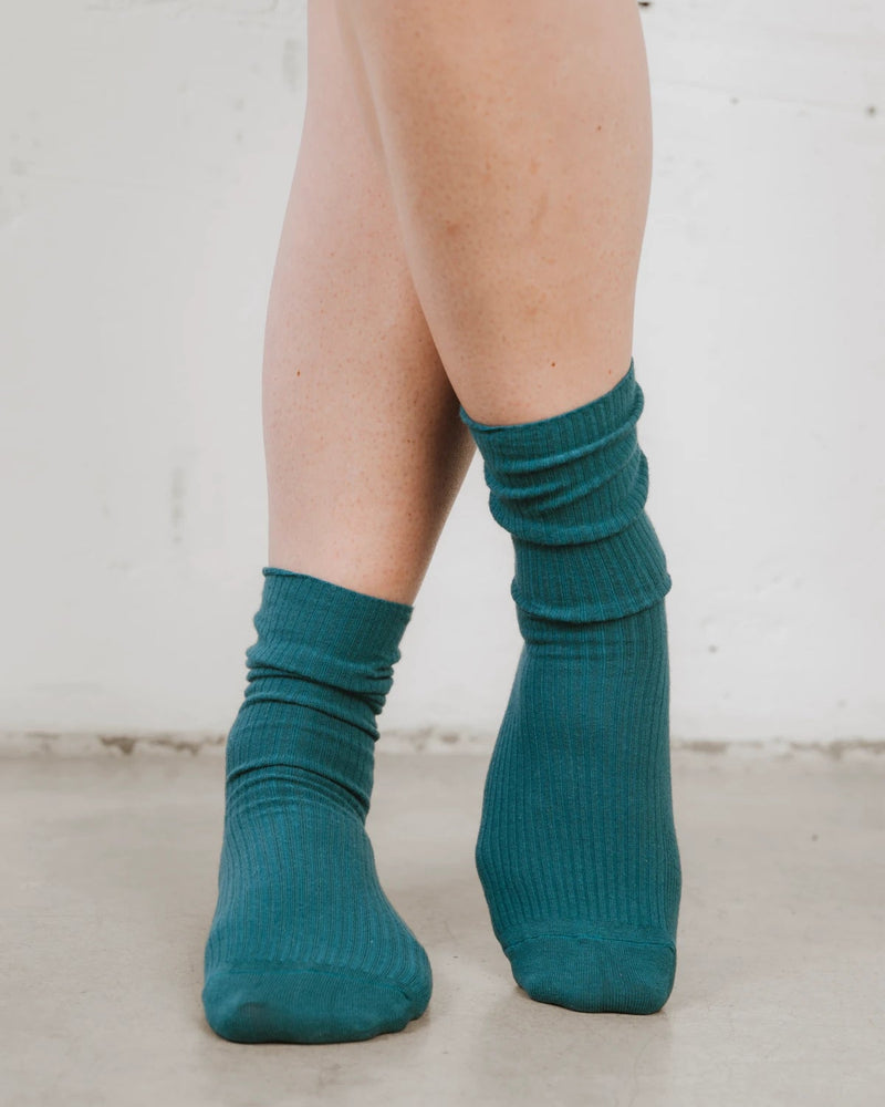 Close-up of a hand adjusting the ribbed knit sock at the ankle. The Ribbed Crew Sock Peacock.