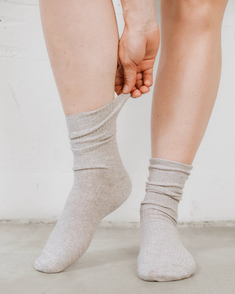 Close-up of a hand pulling up the ribbed knit cuff over the ankle. The Ribbed Crew Sock Grey Melange.