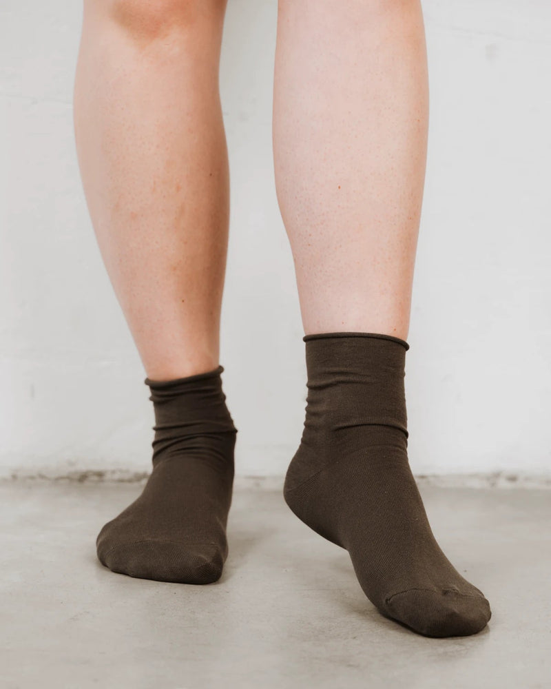 Ankles crossed, showing rolled cuff and soft knit texture. The Daily Mid Crew Sock Olive.