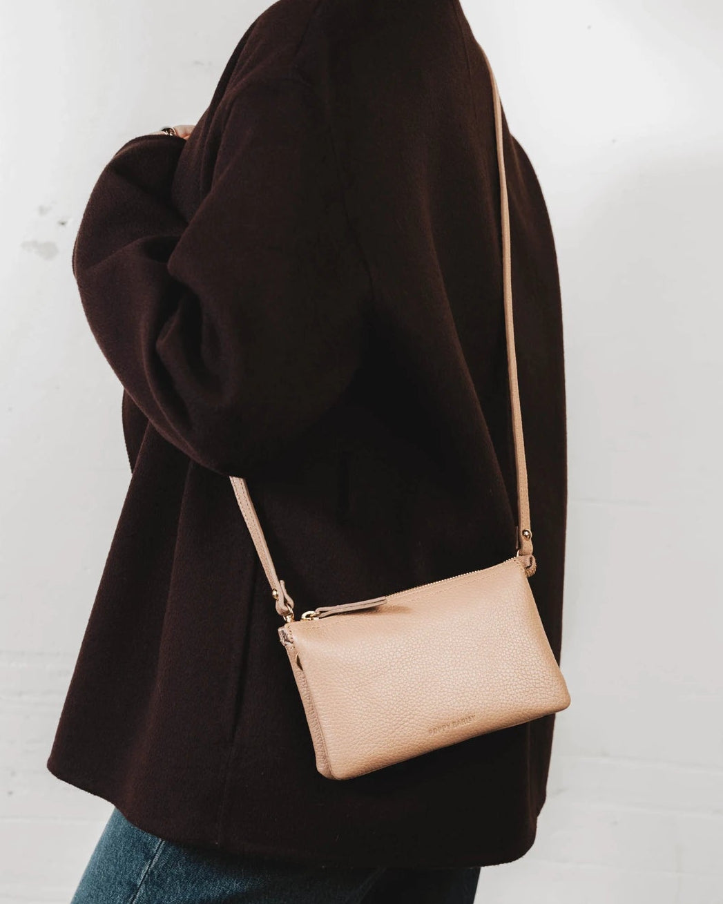 Woman wearing the pebbled-leather wristlet crossbody with a sweater. The 3-in-1 Wristlet Biscotti Pebble.