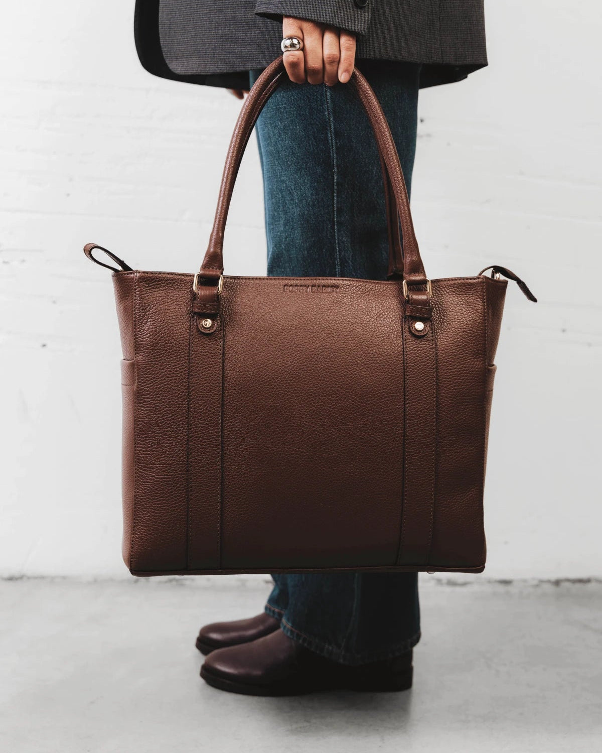Woman carrying the leather tote alongside rain boots. The Colleague Tote French Press.