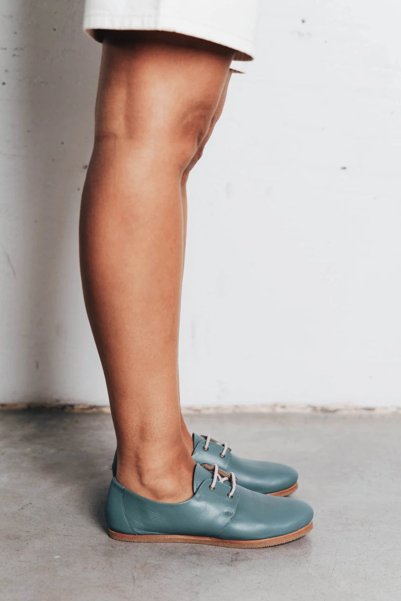 Model's leg shown wearing lace-up oxford flats. The Eyelet Oxford 2.0 Storm. Sizes 5–12, wide available.