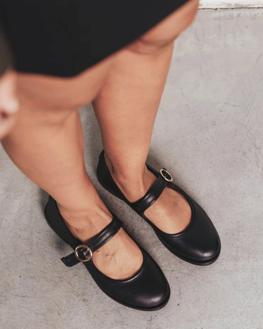 Feet shown wearing round-toe flats with single buckle strap. The Today Mary Jane Black. Sizes 5–12, wide available.