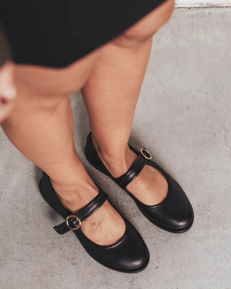 Feet shown wearing round-toe flats with single buckle strap. The Today Mary Jane Black. Sizes 5–12, wide available.