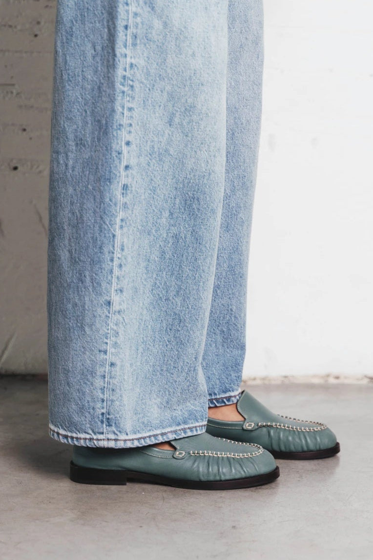 Model's leg shown wearing slip-on loafers with chain trim. The Laid Back Loafer Storm. Sizes 5–12, wide available.