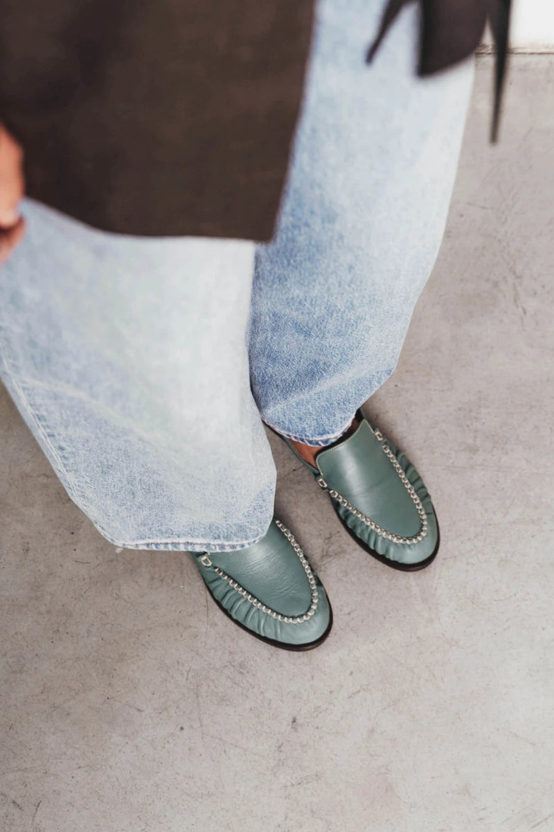 Feet shown wearing slip-on loafers with ruched chain-trim vamp. The Laid Back Loafer Storm. Sizes 5–12, wide available.