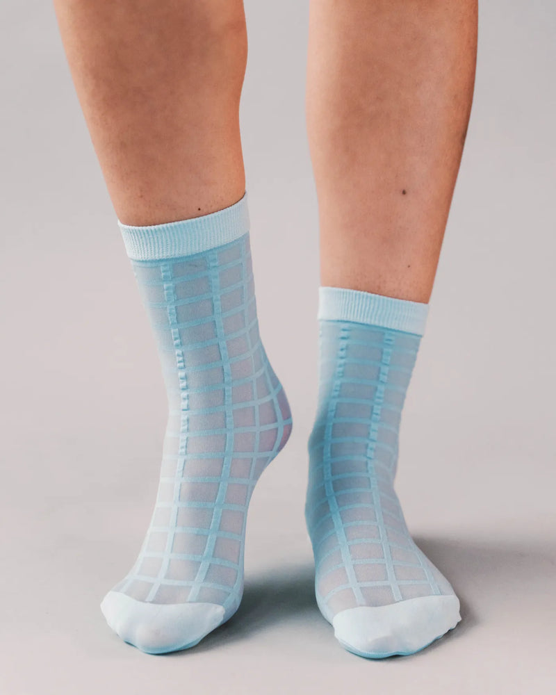 Checkered sheer ankle socks on woman's bare legs. Rachel Checkered Sheer Socks in Sky Blue.