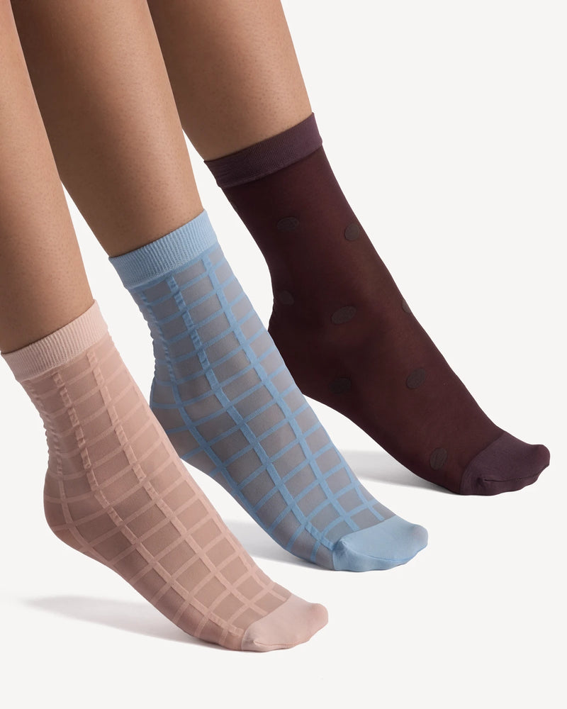 Three pairs of sheer socks in blush, sky blue, and burgundy laid flat on legs. Rachel Sheer Socks 3-Pack.