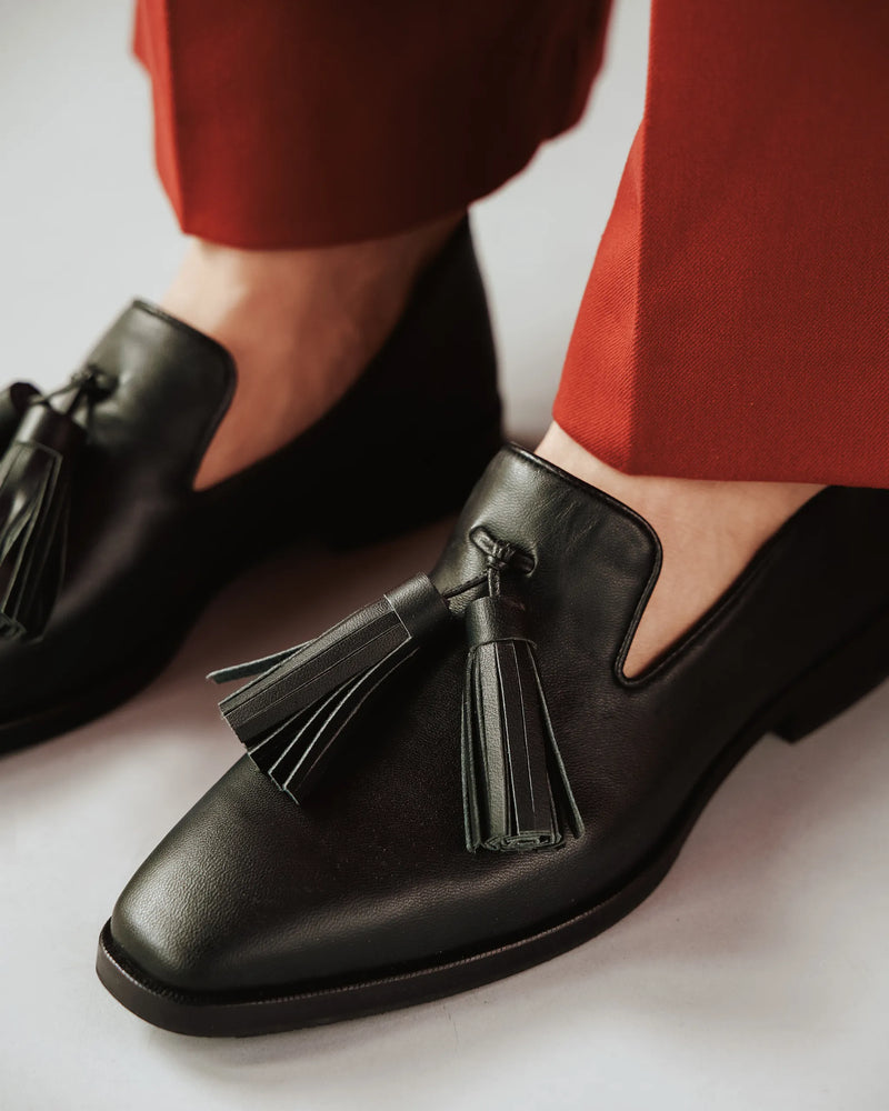 Close-up of leather tassel loafers worn with rust pants. The Tassel Daily Loafer Black. Sizes 5–12, available in wide.
