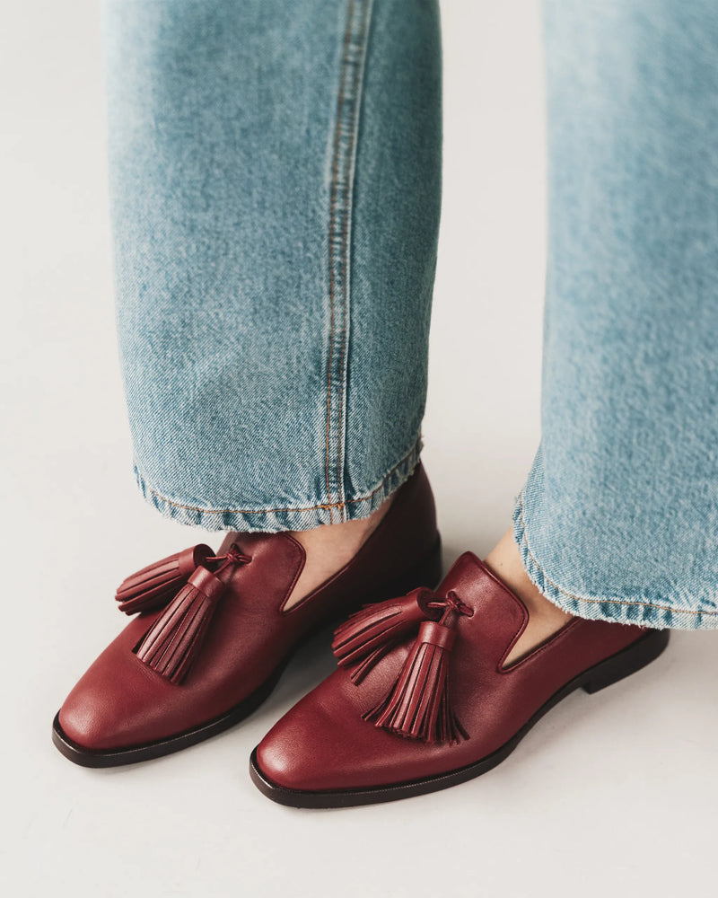 Close-up of resort red tassel loafers worn with jeans. The Tassel Daily Loafer Resort Red. Sizes 5–12, available in wide.