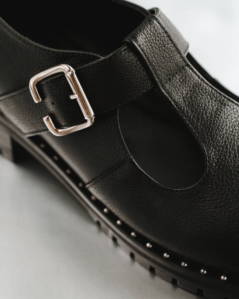 Close-up of pebbled leather T-bar Mary Jane buckle strap and stud sole. The Academy Mary Jane Black. Sizes 5–12.