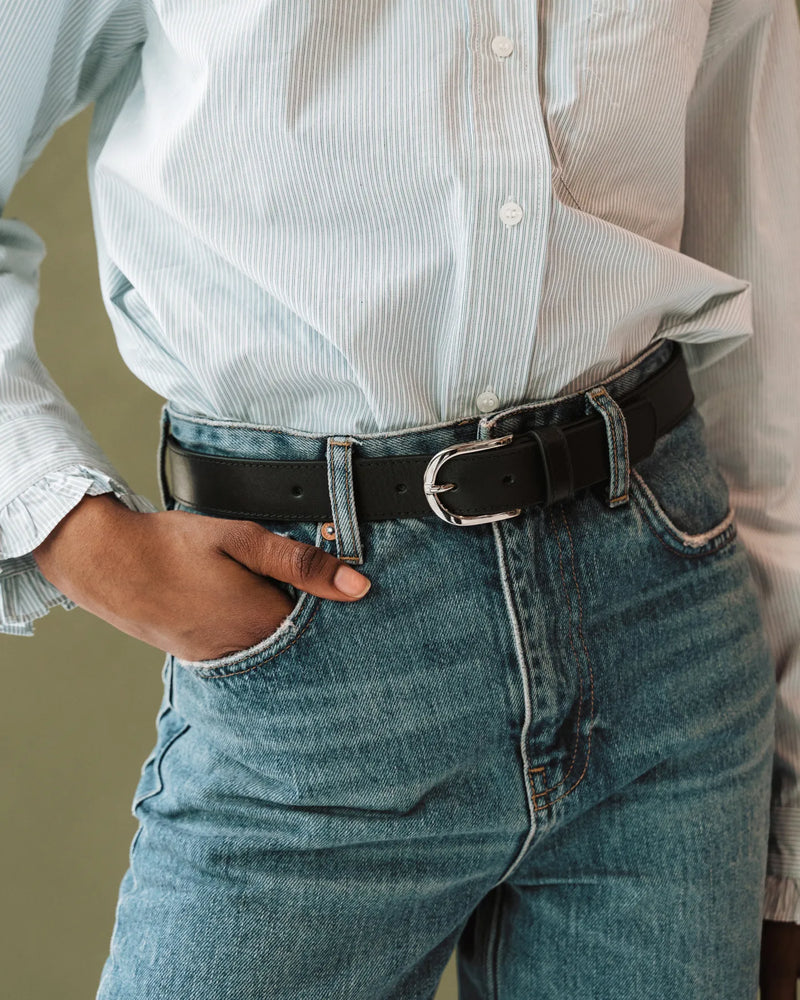 Black smooth leather belt with silver buckle, worn with blue jeans and striped shirt. The Accent Belt Silver Black.