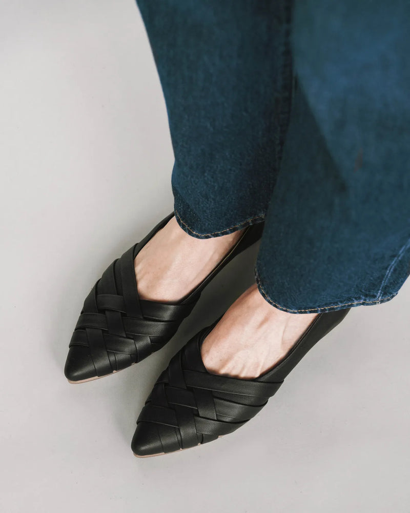 Overhead view of woven leather pointed-toe flats worn with dark blue denim jeans. The Athena Flat Black. Sizes 5–12.