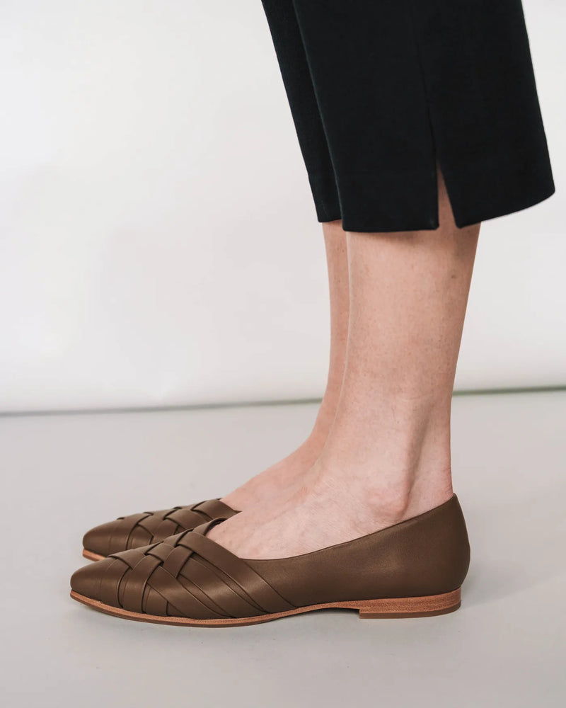 Woven leather pointed-toe flat, worn with black trousers. The Athena Flat Tapenade. Sizes 5–12, available in wide.