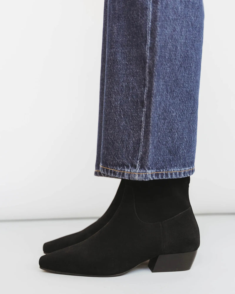 Side view of woman in dark jeans wearing suede square-toe ankle boots with block heel. The Beau Boot Black. Sizes 5–12.