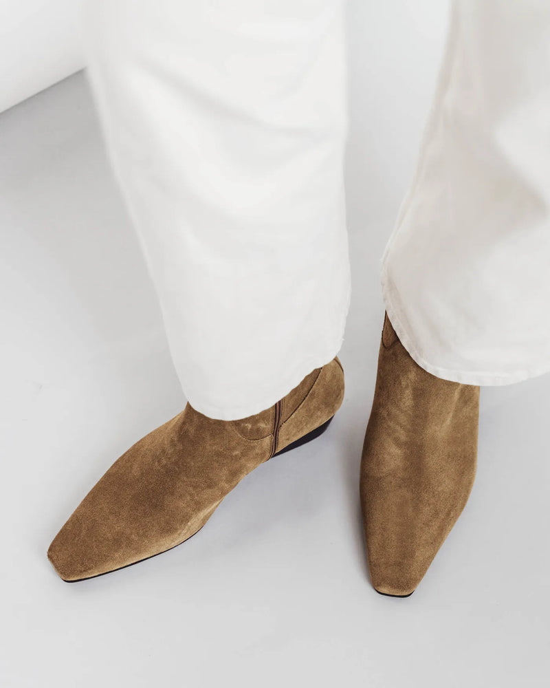 Woman in cream wide-leg pants wearing suede square-toe ankle boots. The Beau Boot Desert Suede. Sizes 5–12.