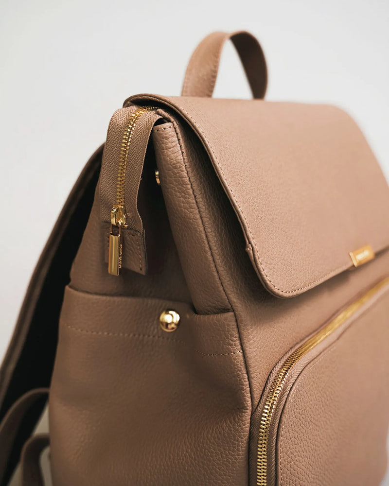 Close-up of the flap top and gold zipper hardware on a pebbled leather backpack. The Beyond Backpack Biscotti.