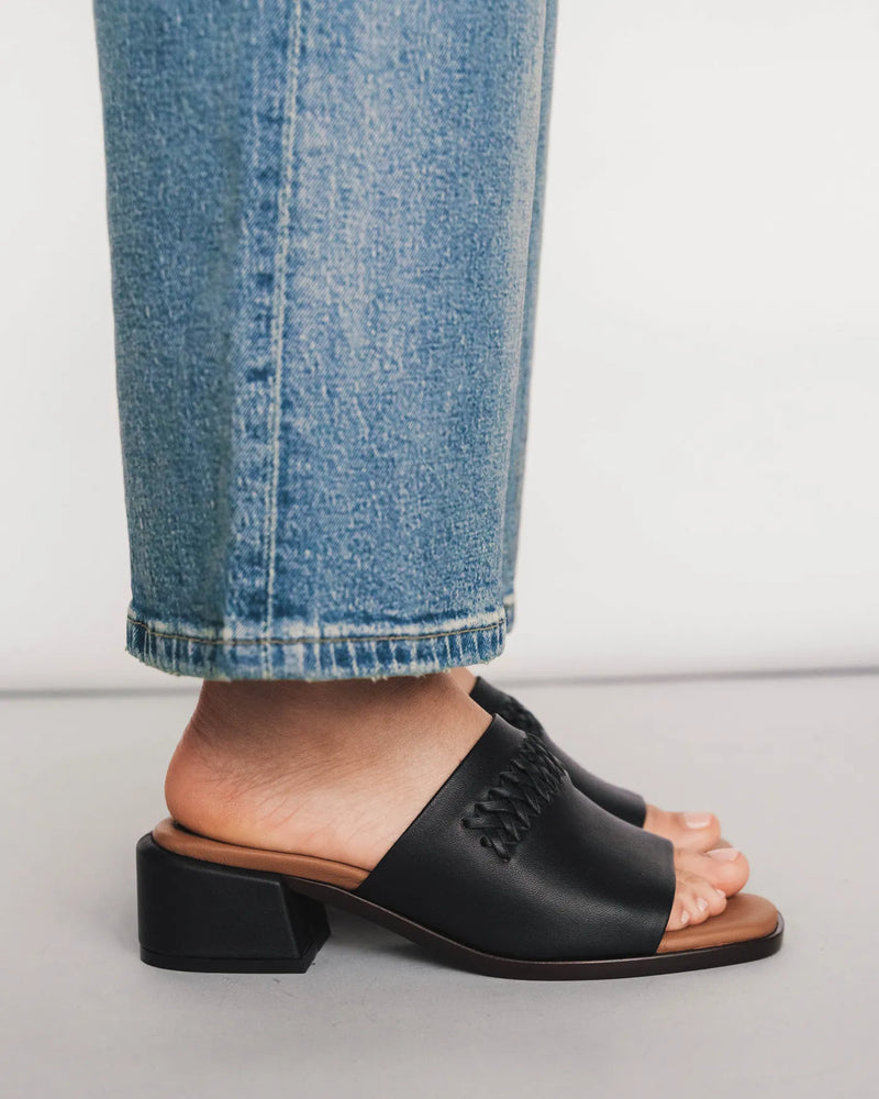 Leather block-heeled slides with woven detail, side view with light jeans. The Bohème Heeled Sandal Black. Sizes 5–12.