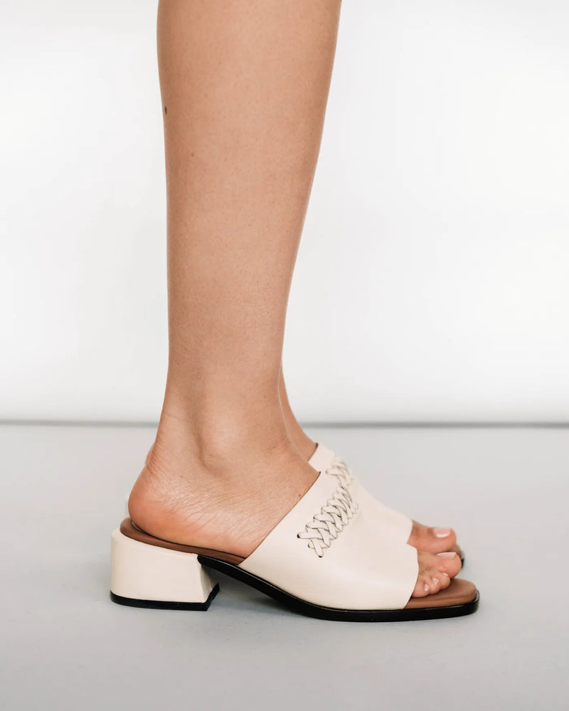 Heeled slides with woven strap detail, side view. The Bohème Heeled Sandal Oat Milk. Sizes 5–12, available in wide.
