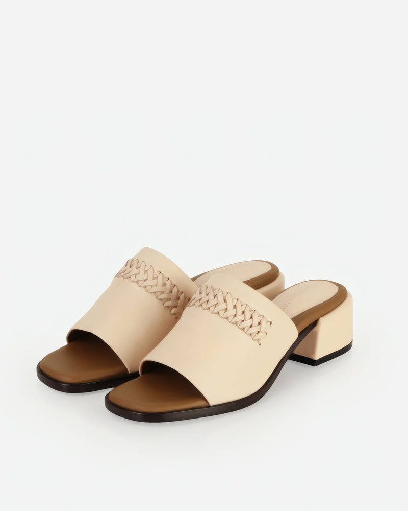 Front-angled pair of heeled slide sandals with woven strap. The Bohème Heeled Sandal Oat Milk. Sizes 5–12.