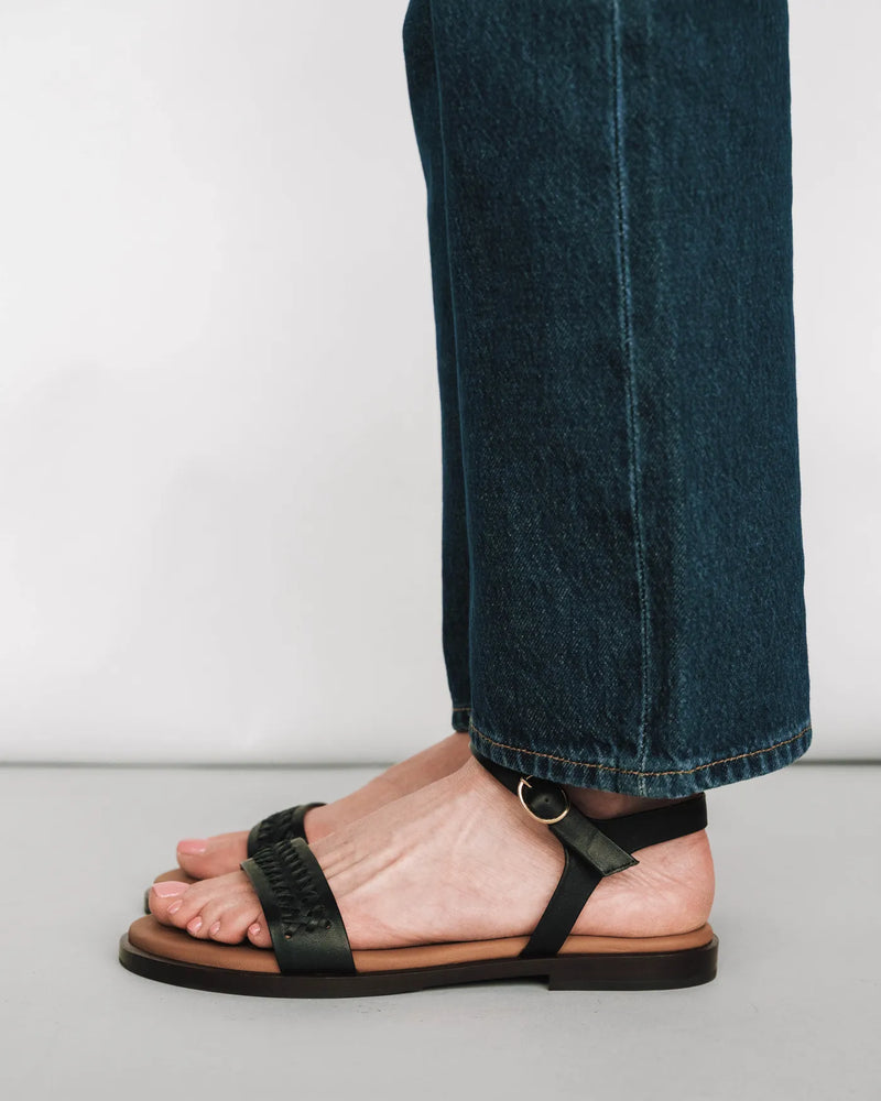 Woven leather sandals with ankle strap, styled with dark jeans. The Bohème Sandal Black. Sizes 5–12, available in wide.
