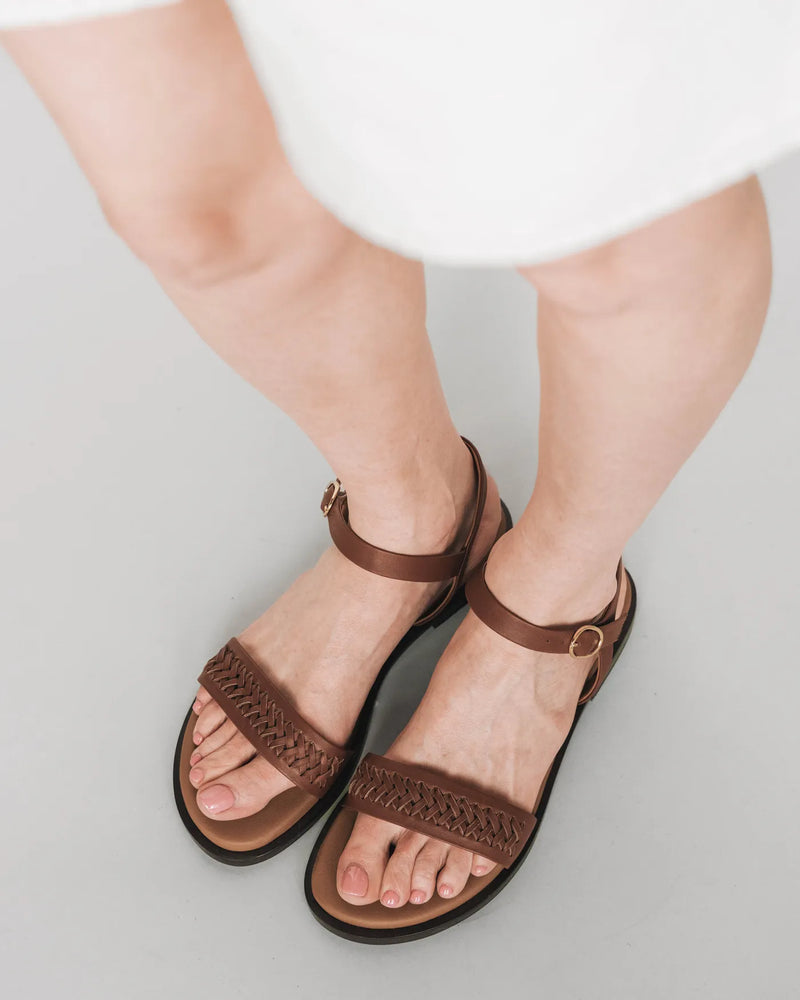 Woven leather sandals with ankle strap, overhead view with white dress. The Bohème Sandal Hazelnut. Sizes 5–12.
