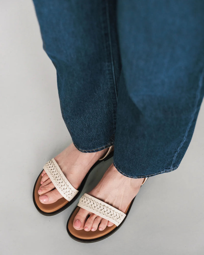 Woven leather sandals with ankle strap, overhead view with dark jeans. The Bohème Sandal Oat Milk. Sizes 5–12.