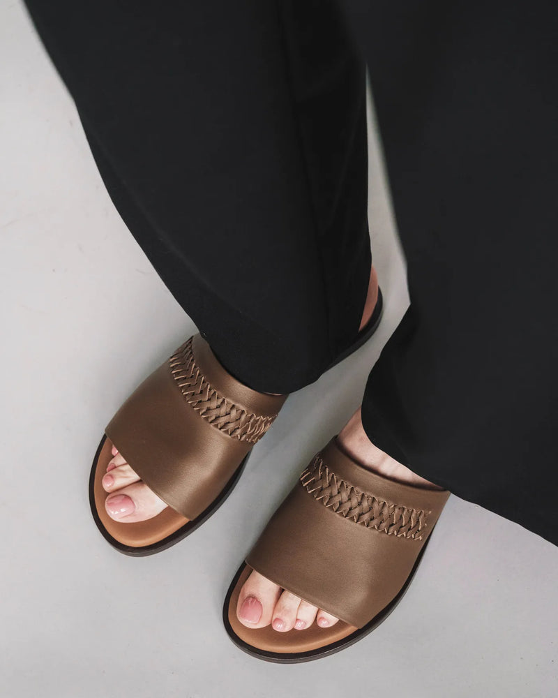 Leather slides with woven detail, worn with black pants. The Bohème Slide Tapenade. Sizes 5–12, available in wide.