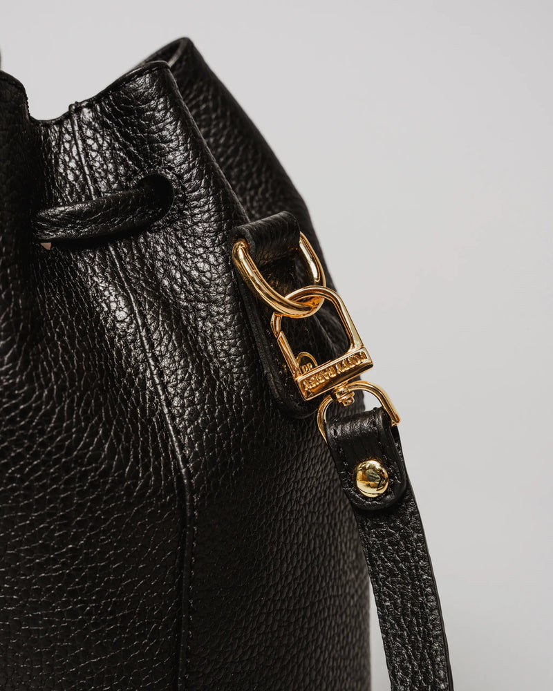 Close-up of gold-tone clasp and ring hardware on a pebbled leather bucket bag. The Bondi Bucket Bag Black.