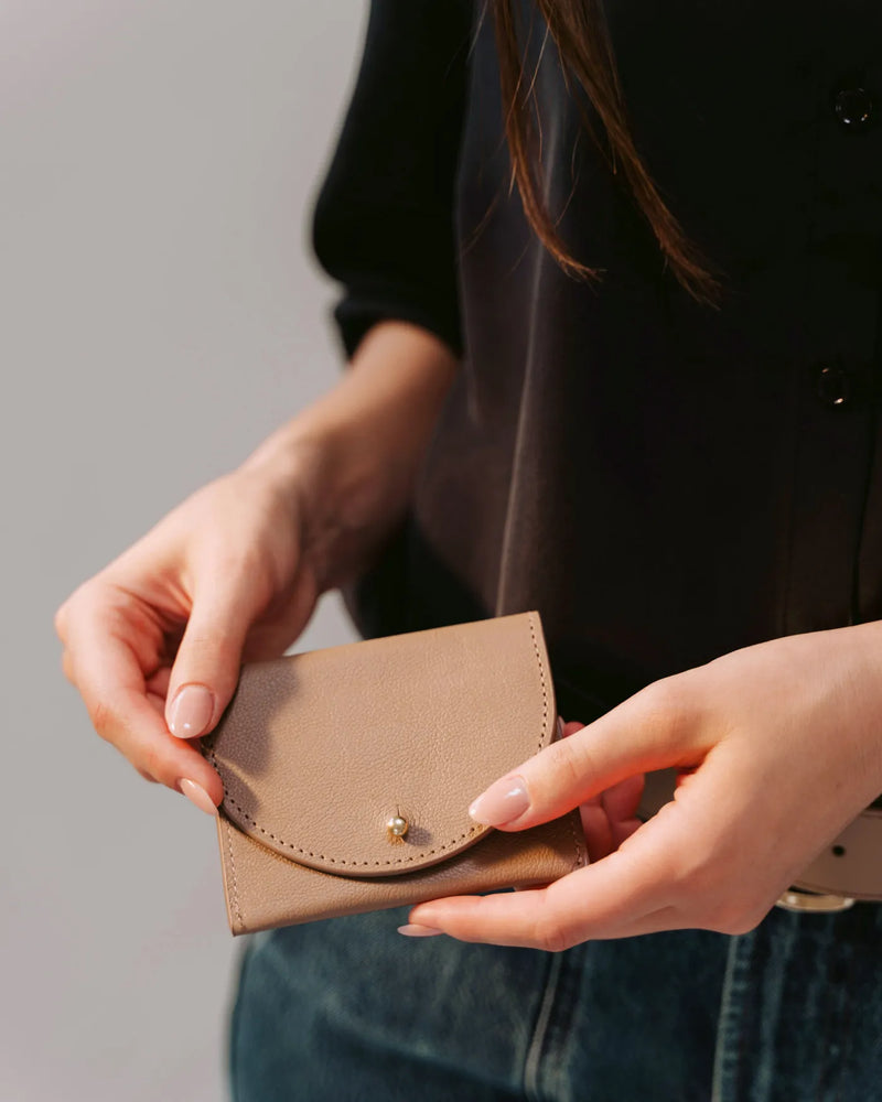 Woman holding biscotti micro pebble cardholder with curved flap and gold stud closure. The Cardholder Biscotti Micro Pebble.