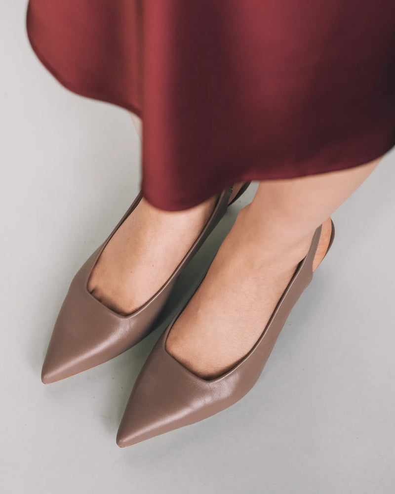 Ceramic leather pointed-toe slingbacks on woman's feet, burgundy satin skirt. The Claire Slingback Ceramic. Sizes 5–12.