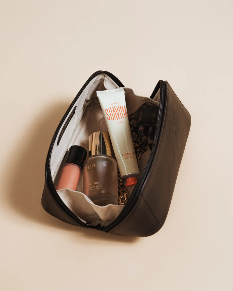 Open leather cosmetic case with canvas interior holding skincare and makeup products. The Cosmetic Case Small Black.
