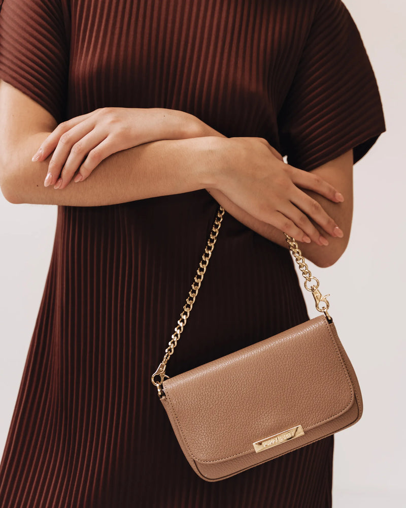 Pebbled leather bag with gold chain, worn by woman in dark ribbed dress. The Day To Night Bag Biscotti Pebble.