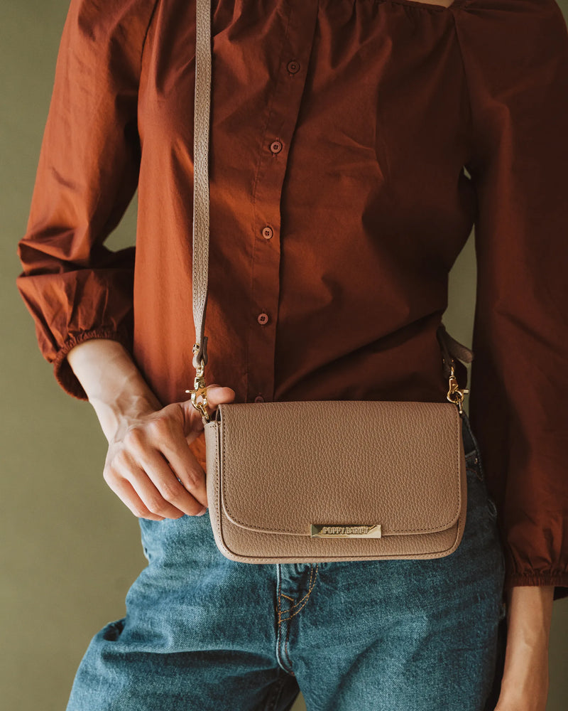 Pebbled leather bag worn crossbody, woman in rust blouse and blue jeans. The Day To Night Bag Biscotti Pebble.