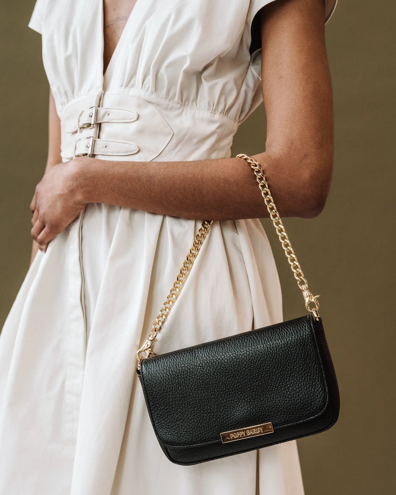 The Day To Night Bag Black Pebble in pebbled leather with gold chain strap, worn by woman in white linen dress