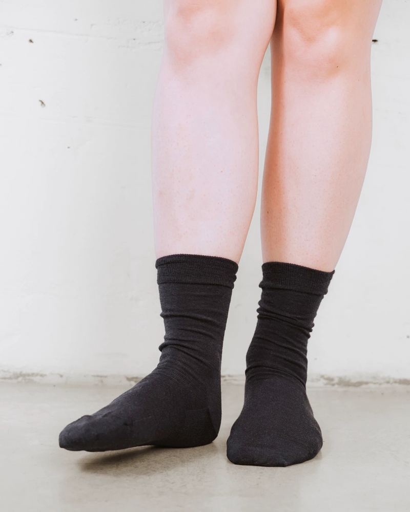 Close-up of hands adjusting the cuff, soft wool knit texture. The Dressy Crew Sock Ink.