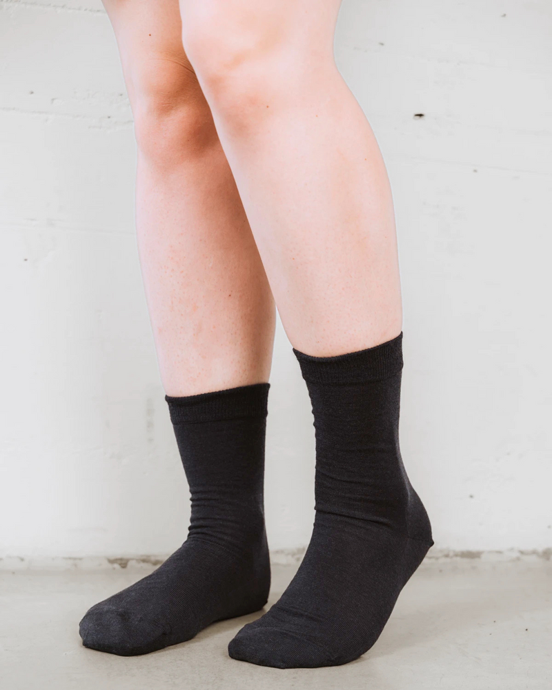 Front view on bare legs, soft wool knit with a rolled cuff. The Dressy Crew Sock Ink.