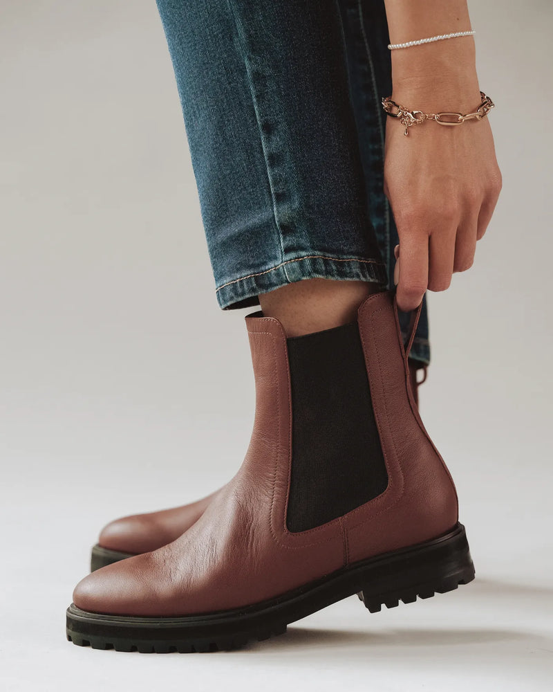 Woman pulling on a leather Chelsea boot with elastic side gore. The Every Way Chelsea Boot Redwood. Sizes 5–12.