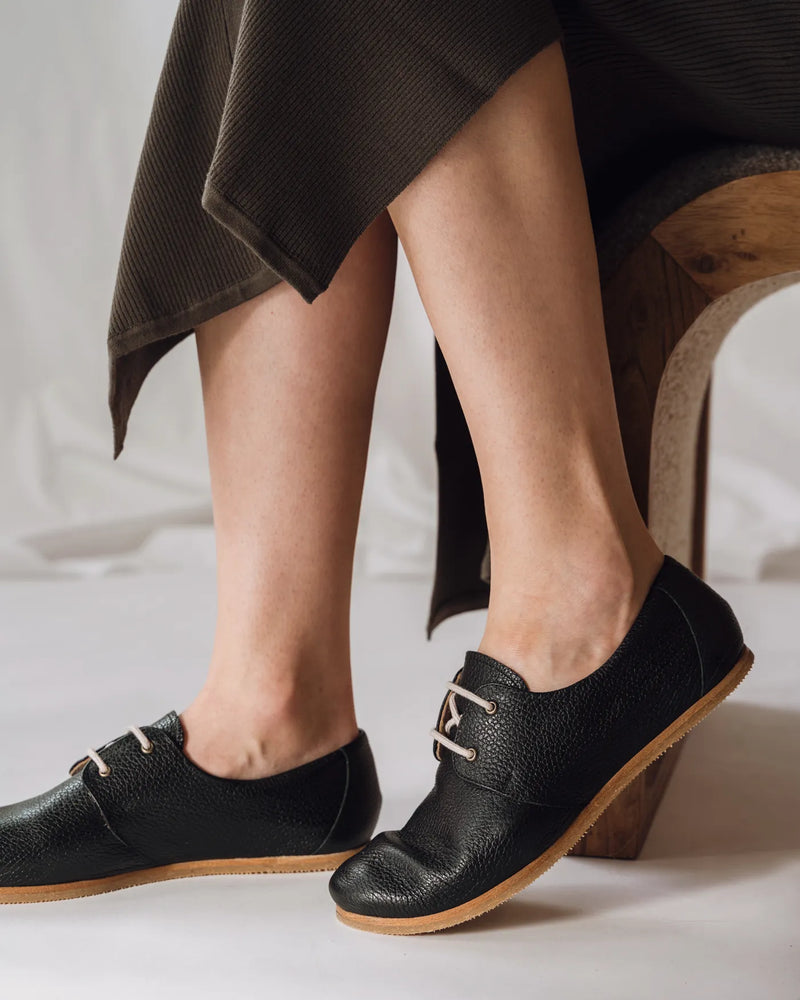 Woman in dark ribbed midi skirt wearing The Eyelet Oxford 2.0 Black Pebble lace-ups. Sizes 5–12, wide available.