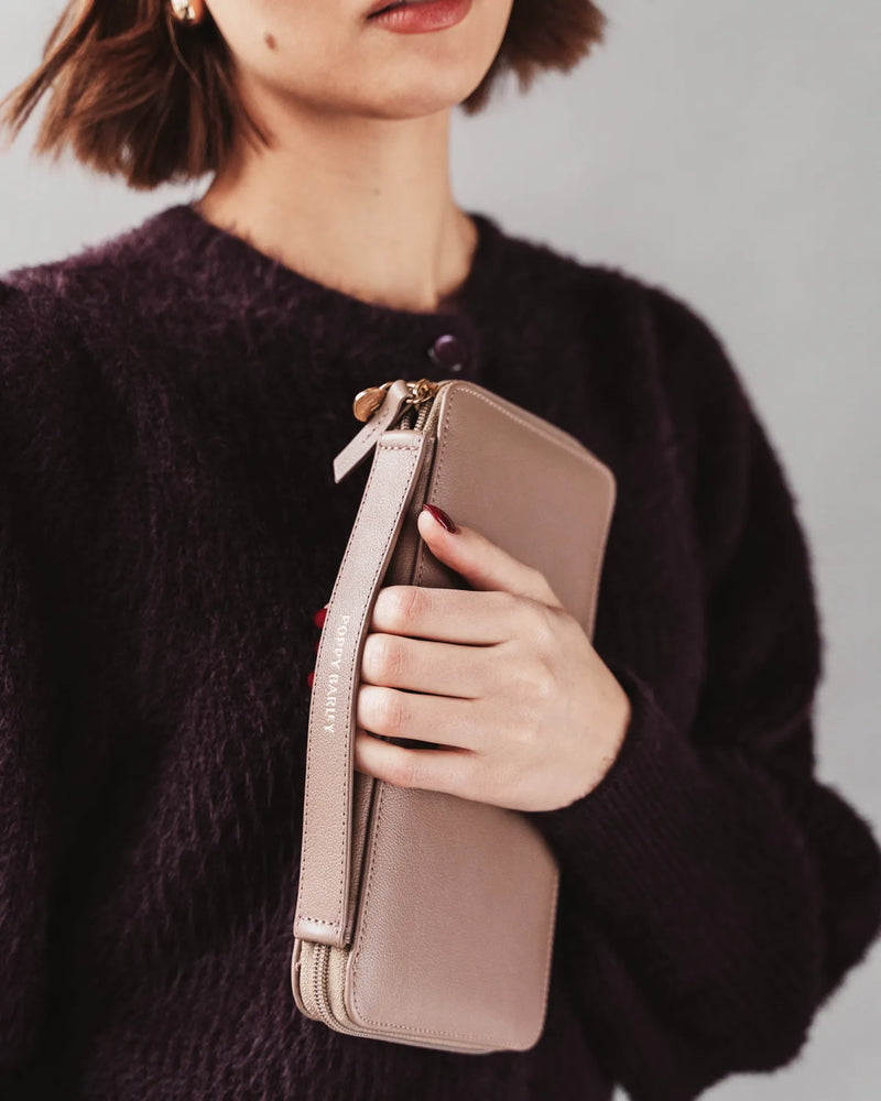The Flying Solo Passport Holder Biscotti Micro Pebble in beige leather, held against chest by woman in aubergine knit