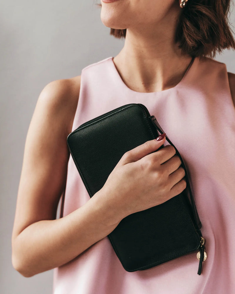 The Four Person Family Passport Holder Pebble in leather, held by woman in pink sleeveless top