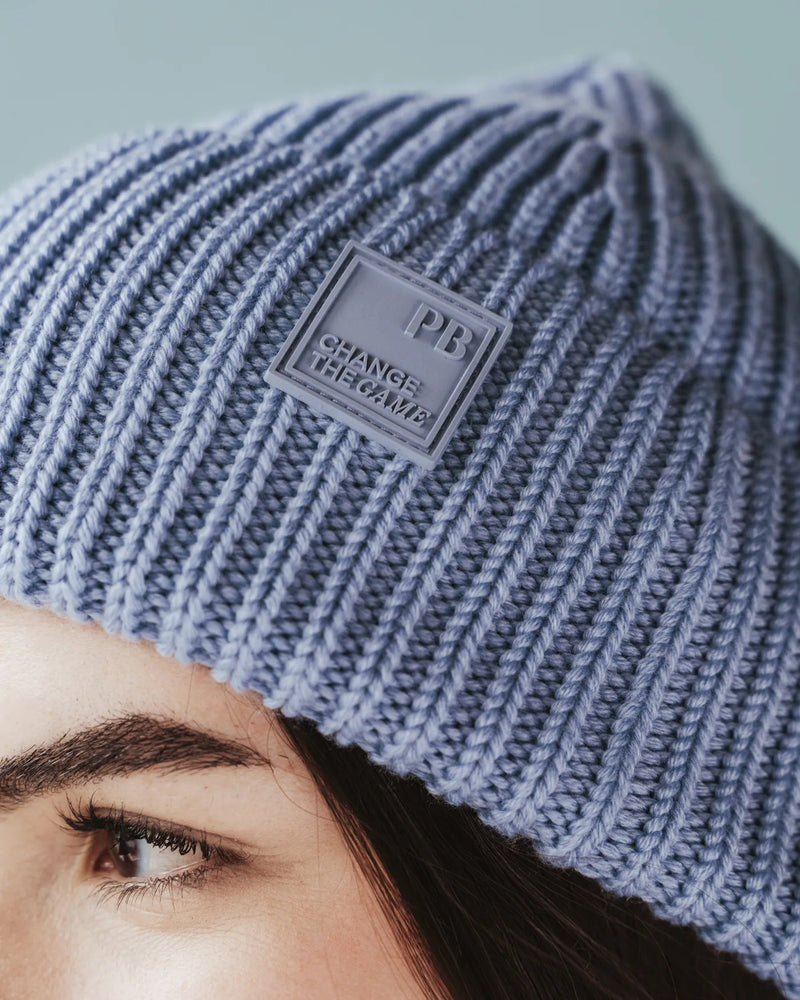 Close-up of woman wearing ice blue ribbed knit beanie with PB rubber patch. The Future Fund Beanie Ice Blue.