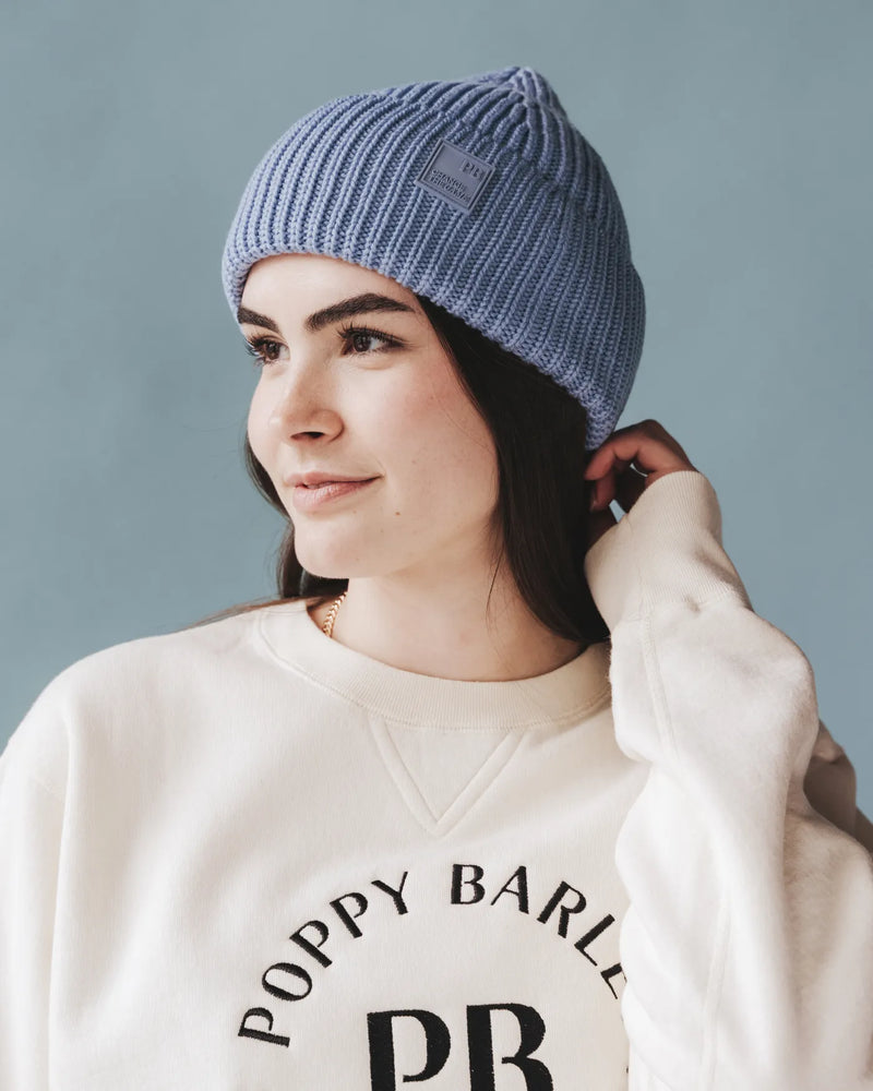 Woman in cream Poppy Barley sweatshirt adjusts ice blue ribbed knit beanie. The Future Fund Beanie Ice Blue.